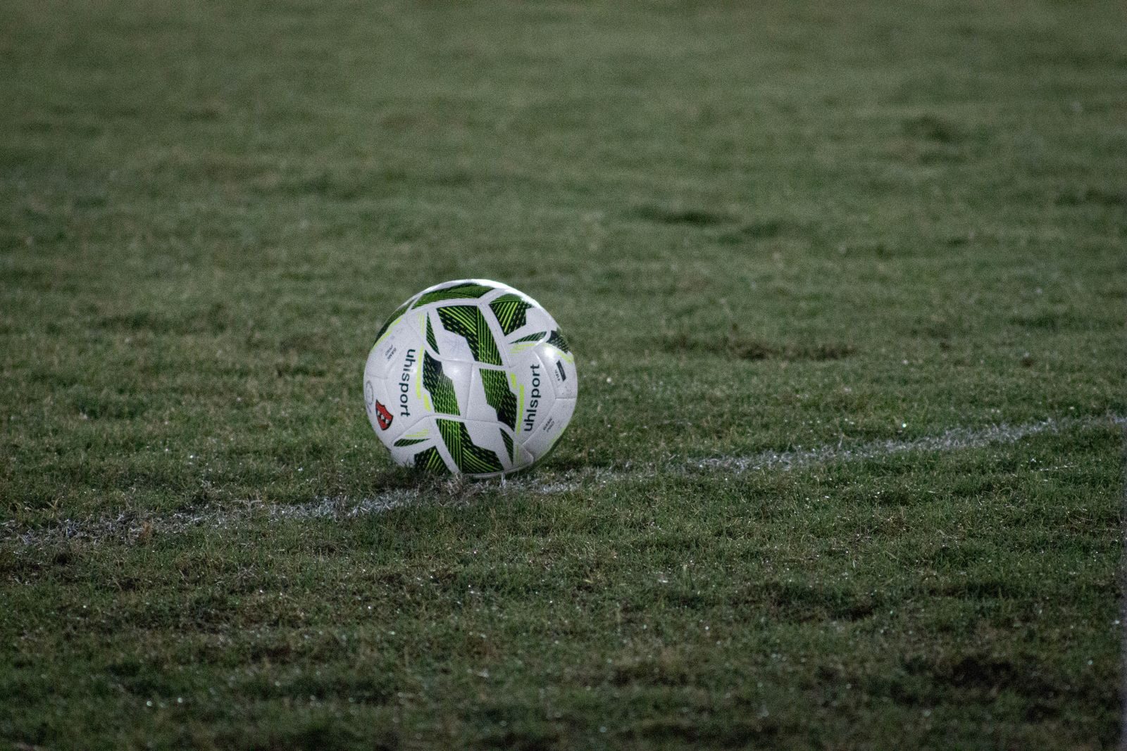 A soccer ball resting on a grass field, captured during nightfall with visible dew.