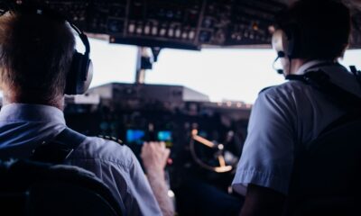 Back view of anonymous male pilots in uniform and headset navigating modern airplane while taking off