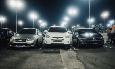 Night scene in a well-lit parking lot featuring various parked cars and street lamps.