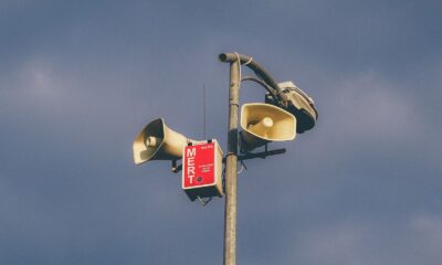 A warning system with loudspeakers on a pole against a cloudy sky, signaling emergency alerts.