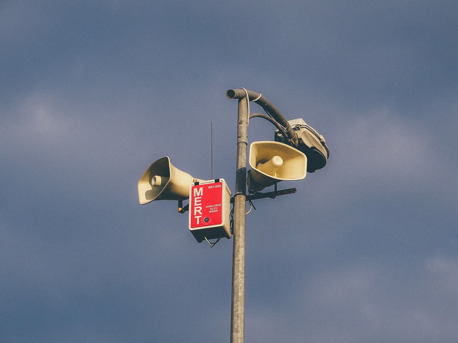 A warning system with loudspeakers on a pole against a cloudy sky, signaling emergency alerts.