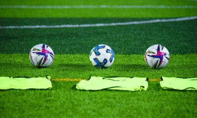 Three soccer balls and training bibs on a lush green field in Rawalpindi, Pakistan.
