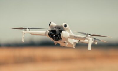White drone flying over a golden field on a clear day, showcasing modern technology.