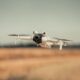 White drone flying over a golden field on a clear day, showcasing modern technology.