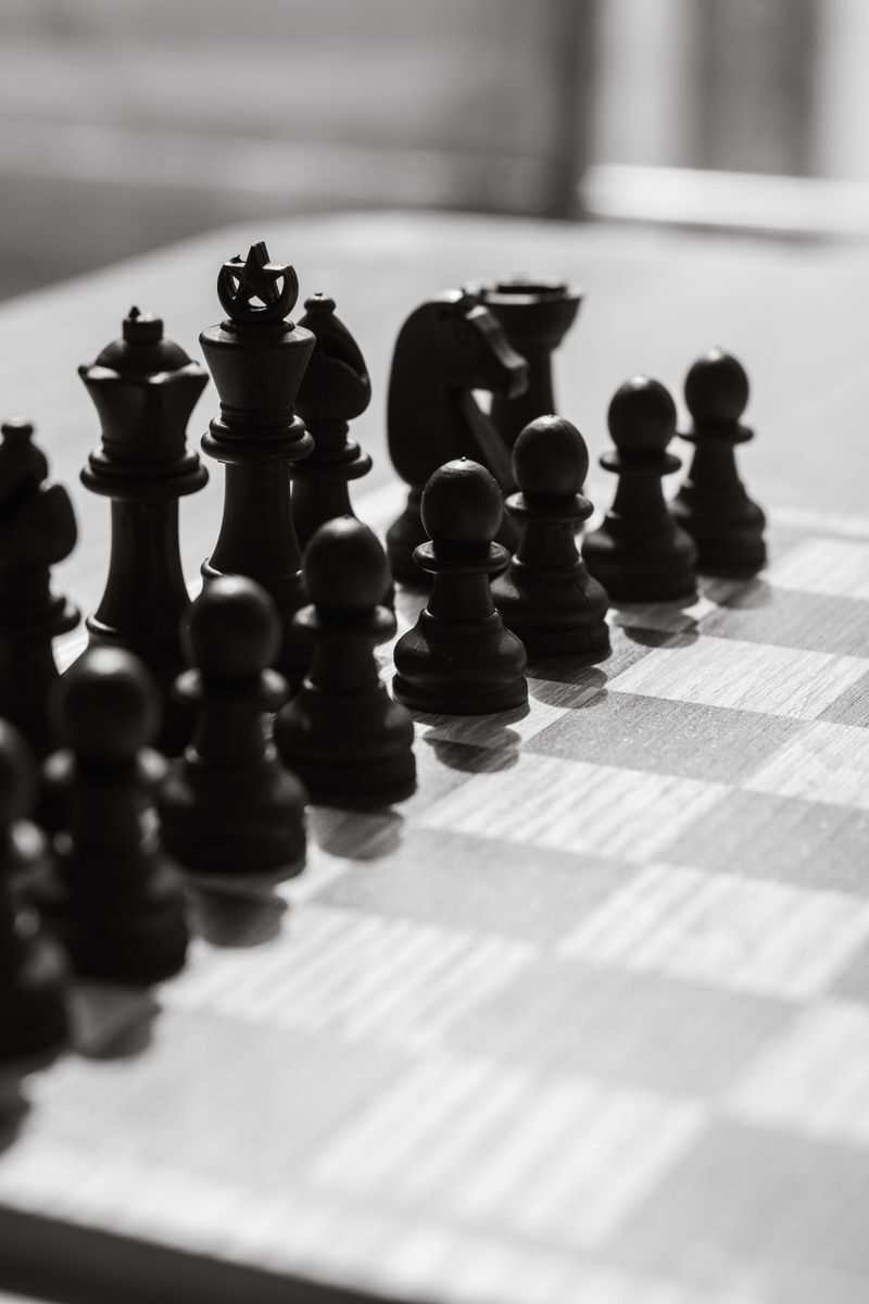 Black and white photo of chess pieces arranged on a chessboard, capturing strategic anticipation.