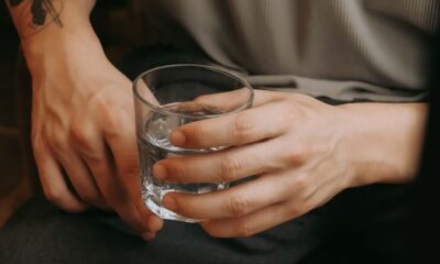A seated man with tattooed arm holding a glass of water, indoors setting.
