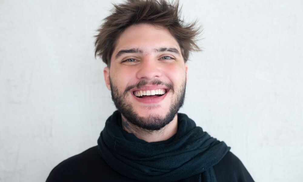 Cheerful young man with a beard smiling warmly, wearing a scarf.