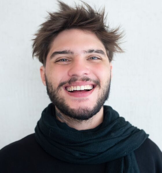 Cheerful young man with a beard smiling warmly, wearing a scarf.