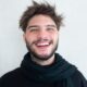 Cheerful young man with a beard smiling warmly, wearing a scarf.