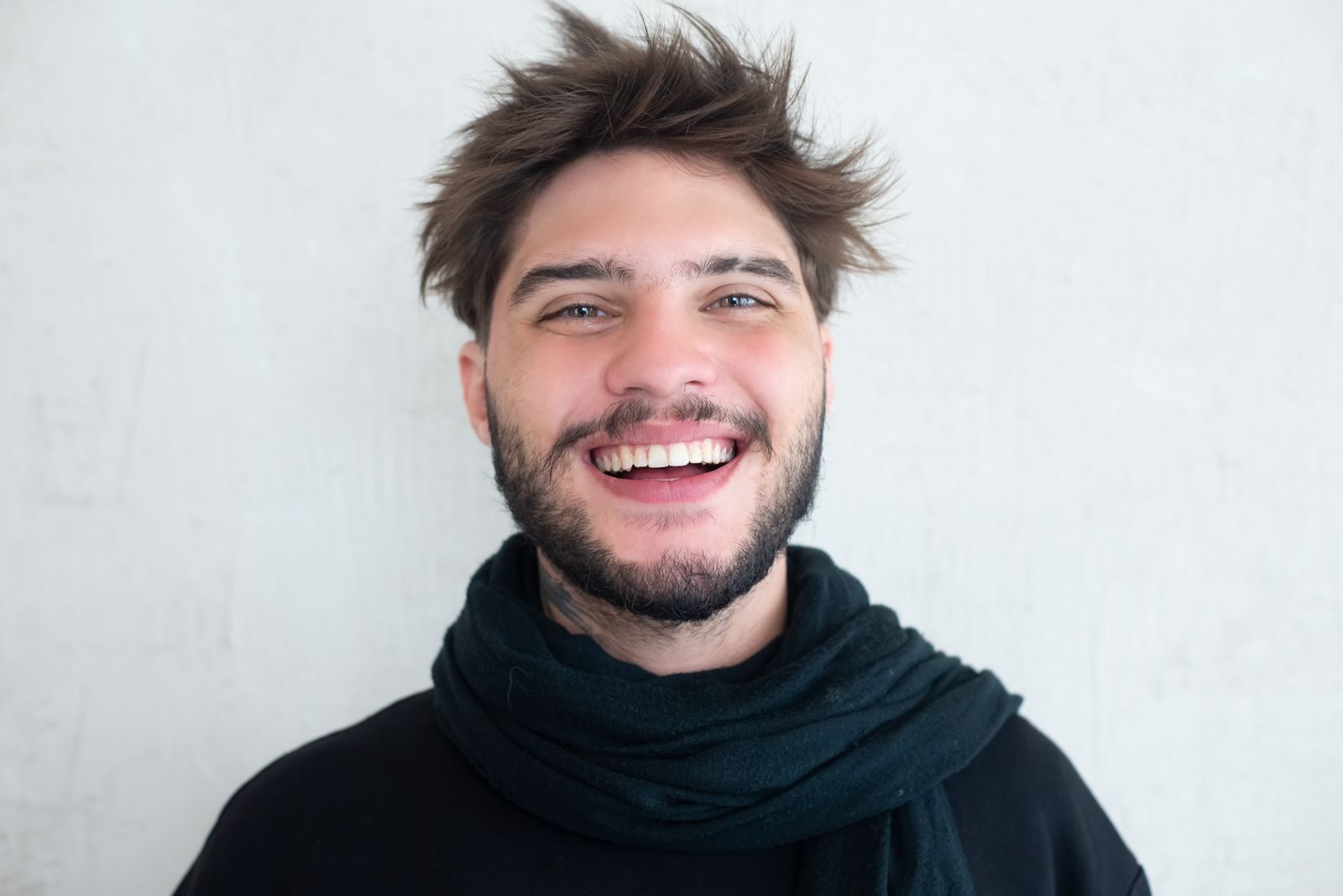 Cheerful young man with a beard smiling warmly, wearing a scarf.