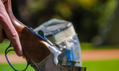 Detailed view of a shotgun ejecting spent shells during target practice in a grassy outdoor area.