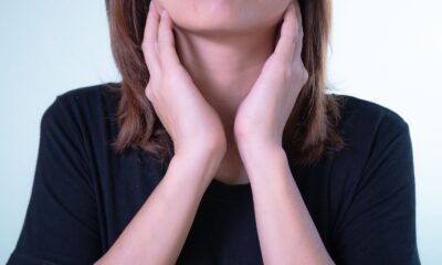 Close-up of a woman touching her neck, possibly indicating discomfort or throat pain.