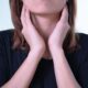 Close-up of a woman touching her neck, possibly indicating discomfort or throat pain.