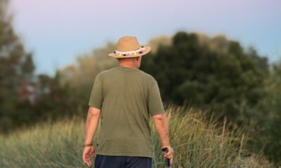 Man in green shirt and hat walking on a rural path with a stick at sunset.