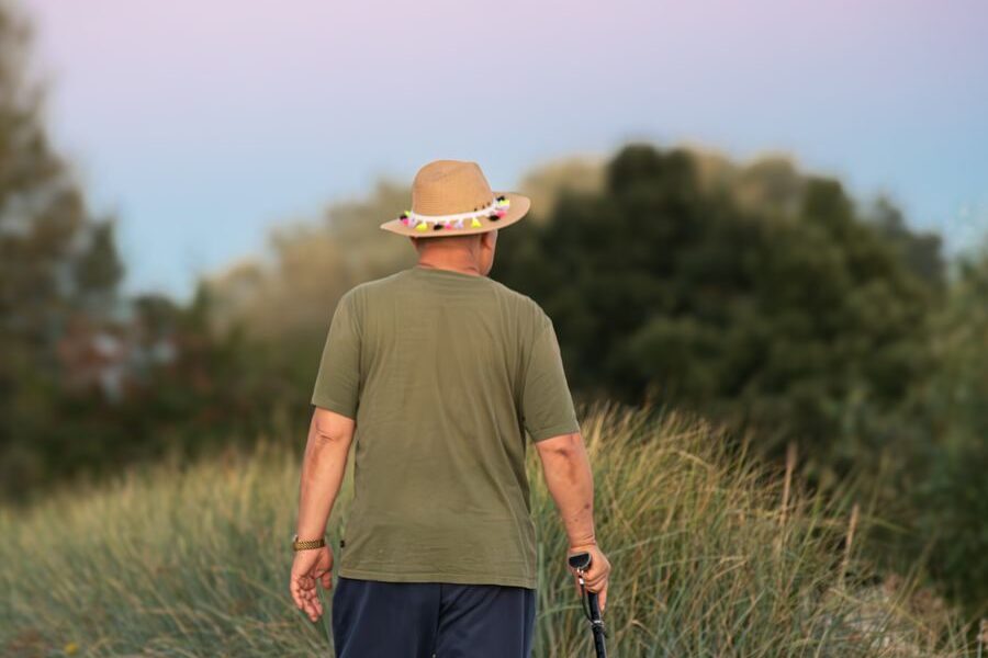 Man in green shirt and hat walking on a rural path with a stick at sunset.
