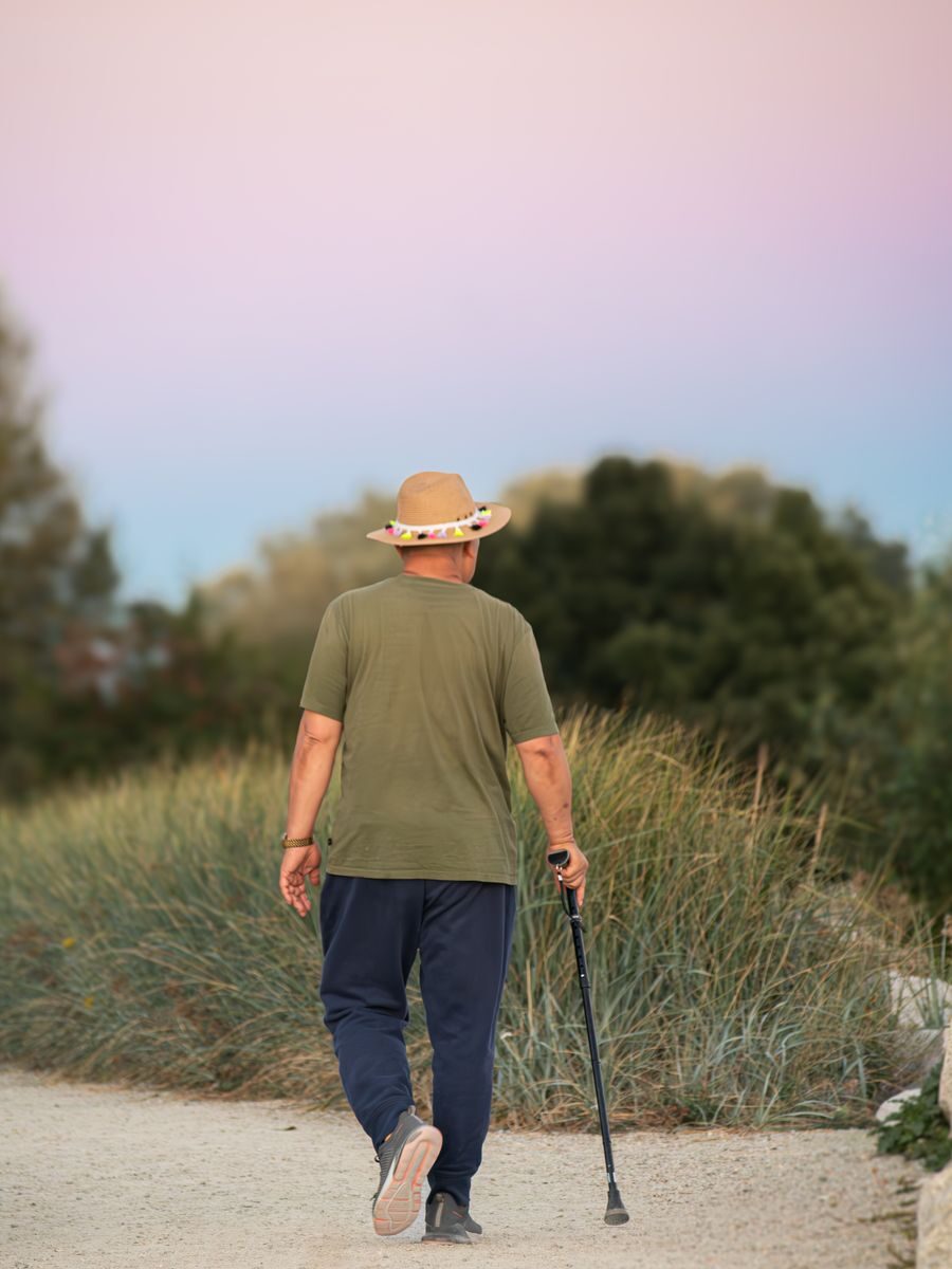 Man in green shirt and hat walking on a rural path with a stick at sunset.