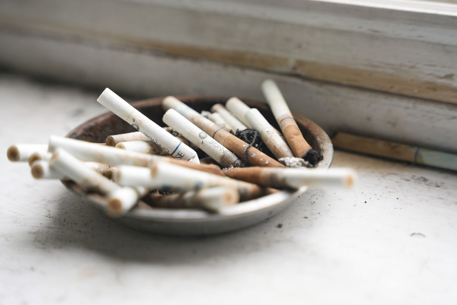 A close-up of an ashtray filled with cigarette butts on a white surface, symbolizing smoking habits.