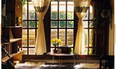 A warm and inviting living room featuring large windows, wooden furniture, and natural light streaming through curtains.