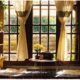 A warm and inviting living room featuring large windows, wooden furniture, and natural light streaming through curtains.