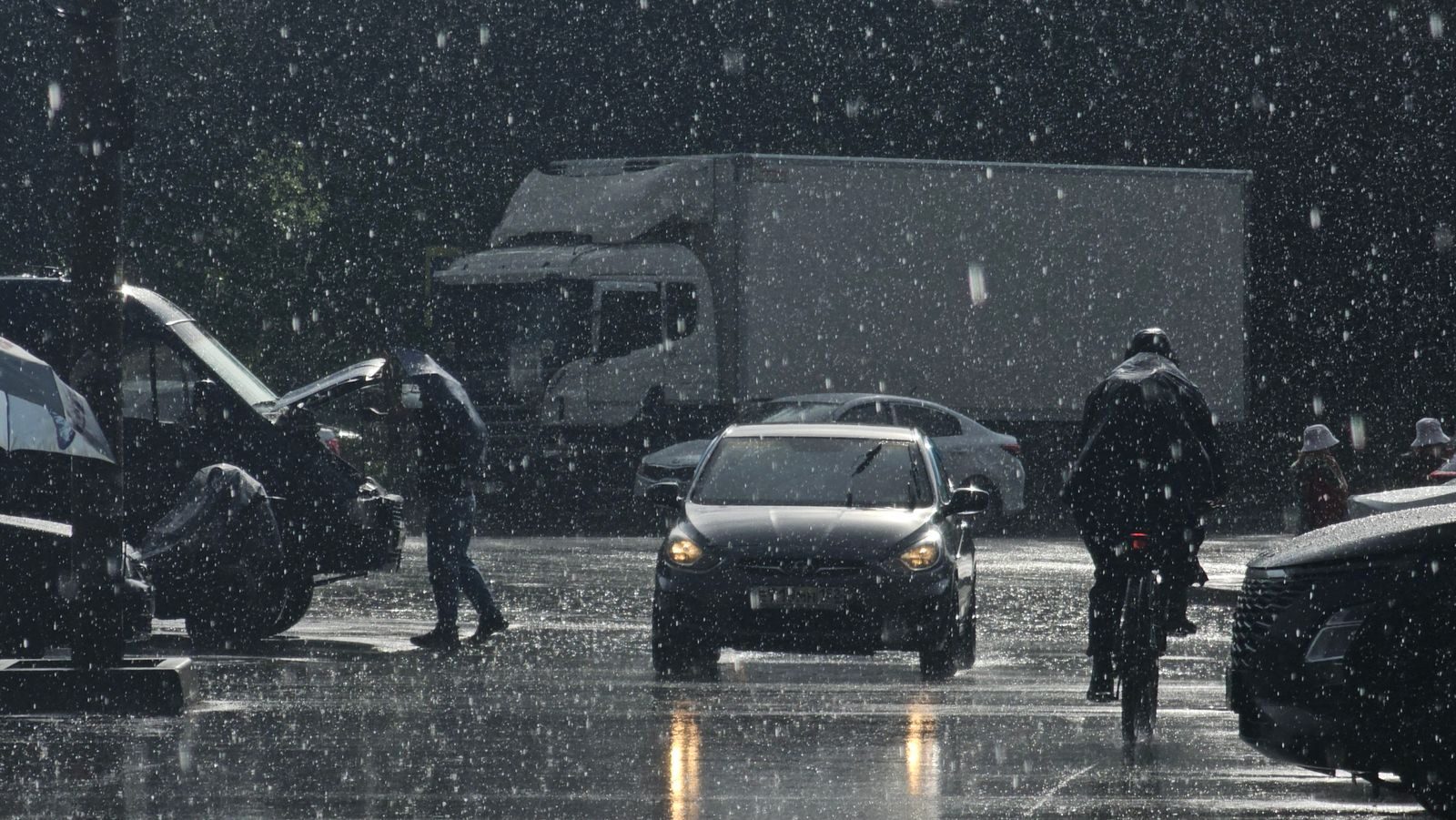 Moody urban street scene in heavy rain with cars and pedestrians.