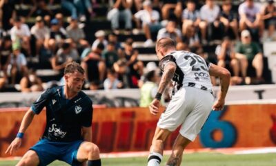 Two soccer players in action during a match with a crowd in the stands on a sunny day.