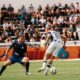 Two soccer players in action during a match with a crowd in the stands on a sunny day.