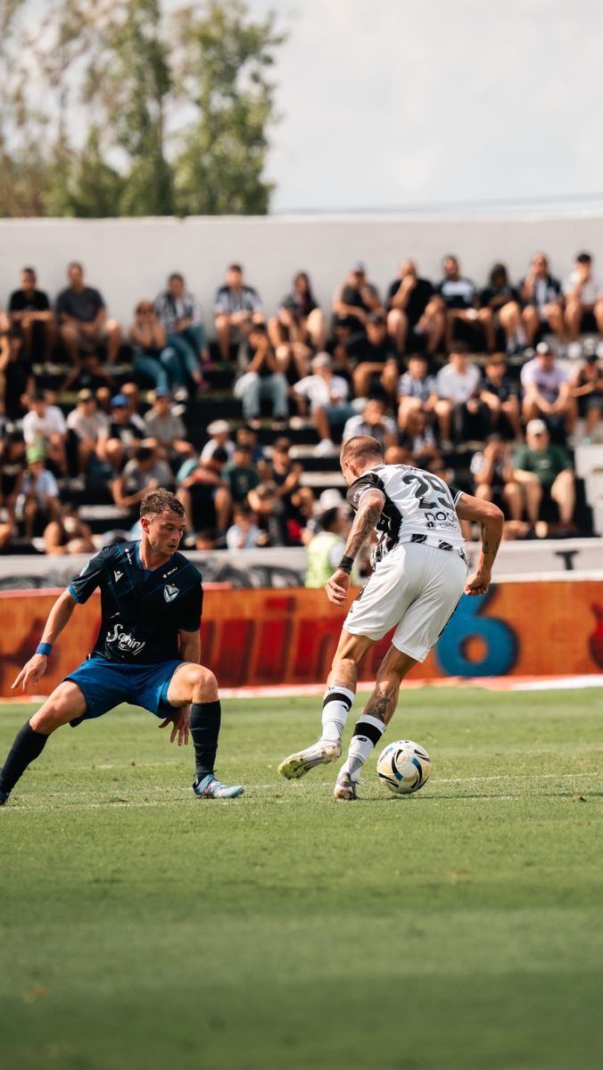 Two soccer players in action during a match with a crowd in the stands on a sunny day.