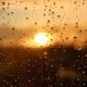 Close-up of raindrops on a window with a stunning golden sunset in the background.