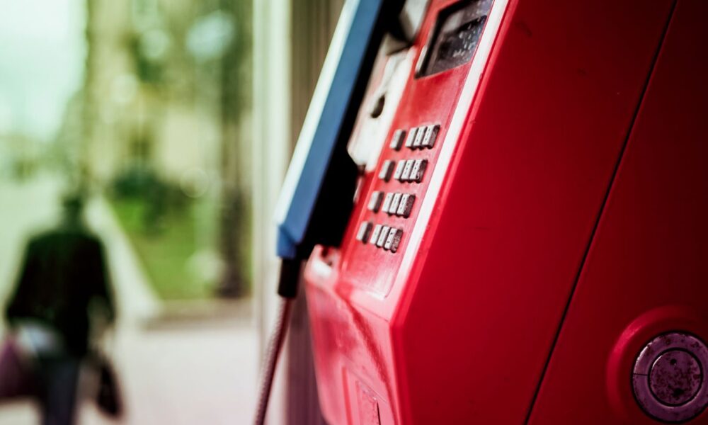 Vibrant red public telephone booth in urban setting with blurred background.