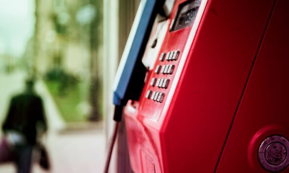 Vibrant red public telephone booth in urban setting with blurred background.