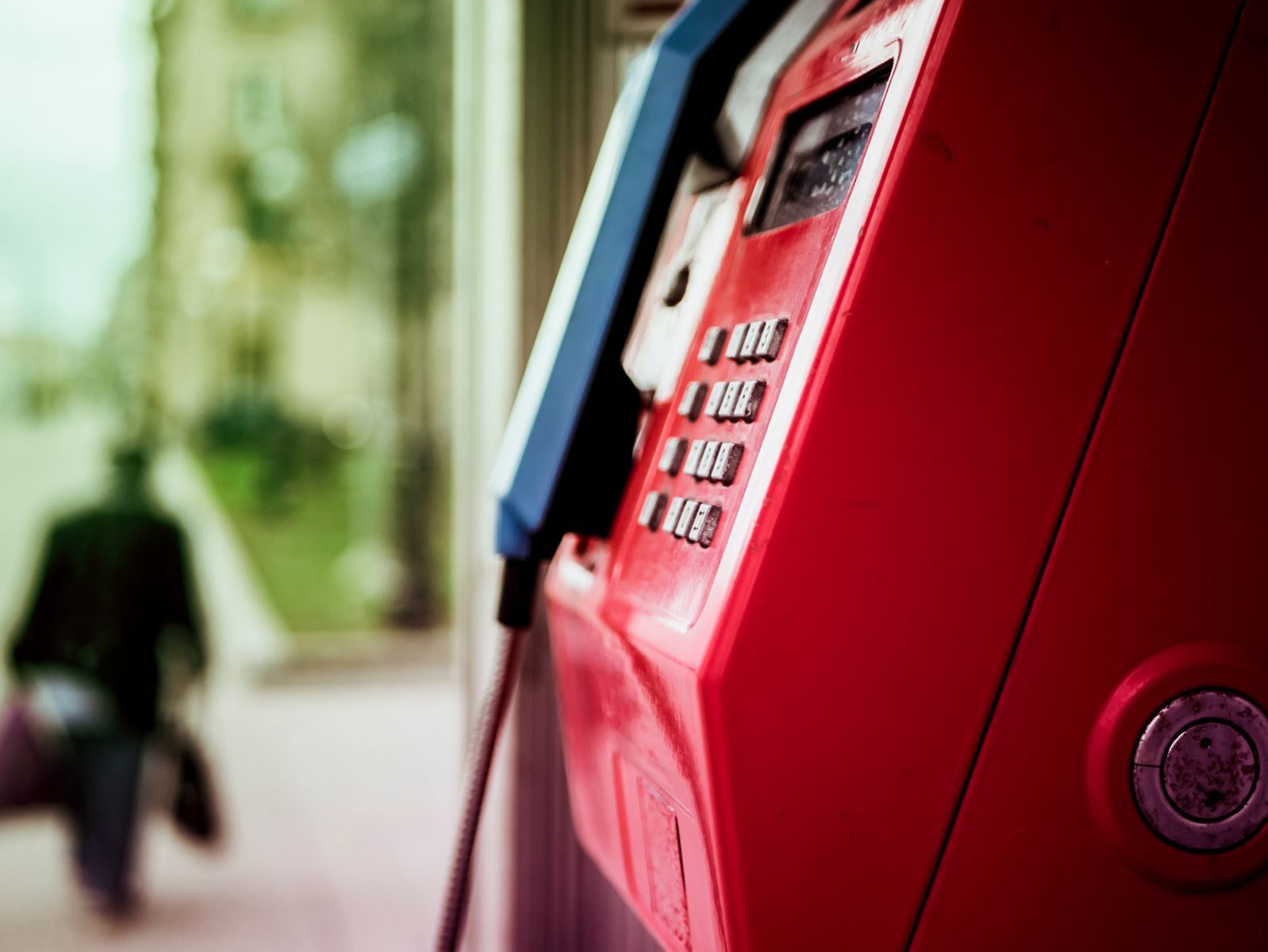 Vibrant red public telephone booth in urban setting with blurred background.