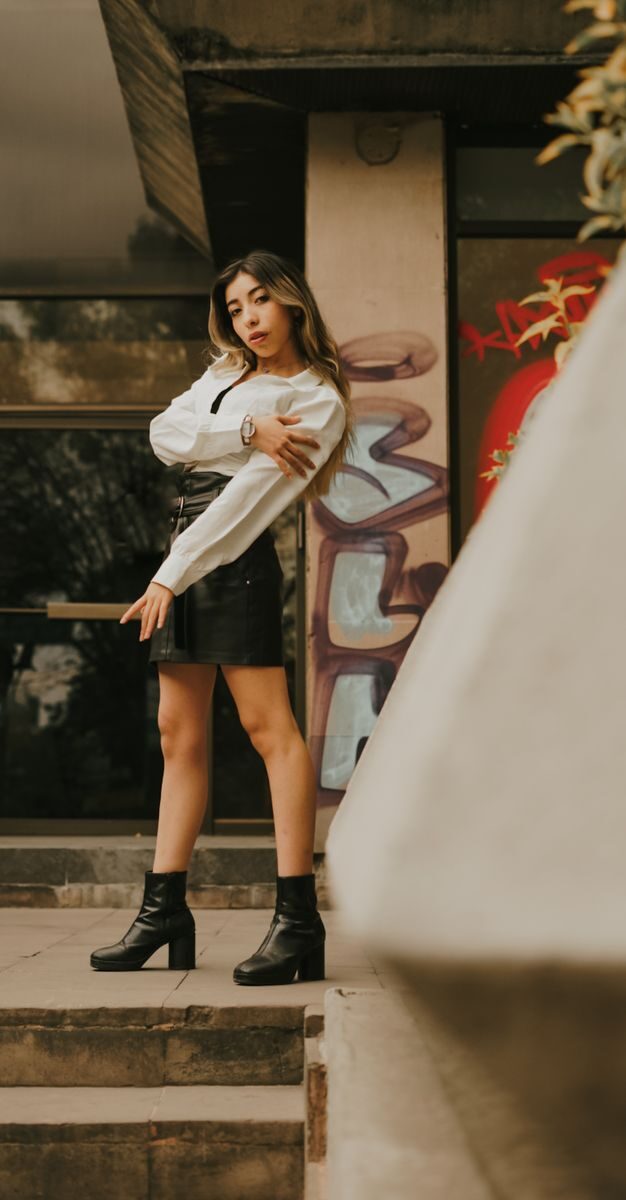 Stylish woman in leather skirt against graffiti wall in urban environment.