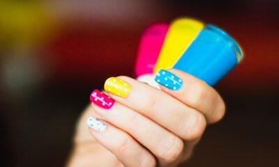 Close-up of a hand with colorful polka dot nail art holding vibrant nail polish bottles.