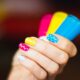Close-up of a hand with colorful polka dot nail art holding vibrant nail polish bottles.