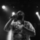 Black and white image of a bearded musician singing live with dynamic lighting.