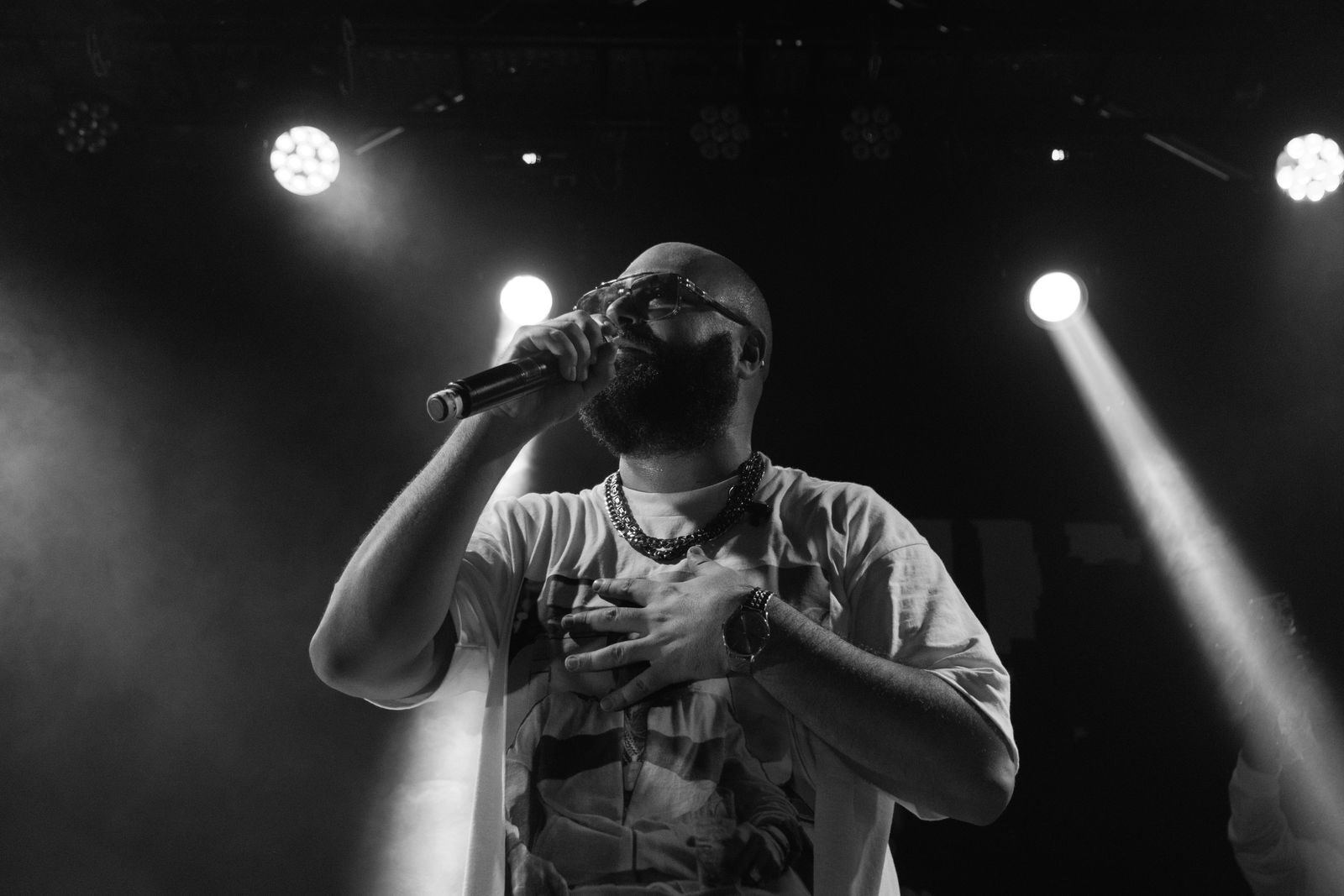 Black and white image of a bearded musician singing live with dynamic lighting.