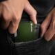 Close-up of a hand holding a minimalist green metal wallet, perfect for everyday carry fashion enthusiasts.