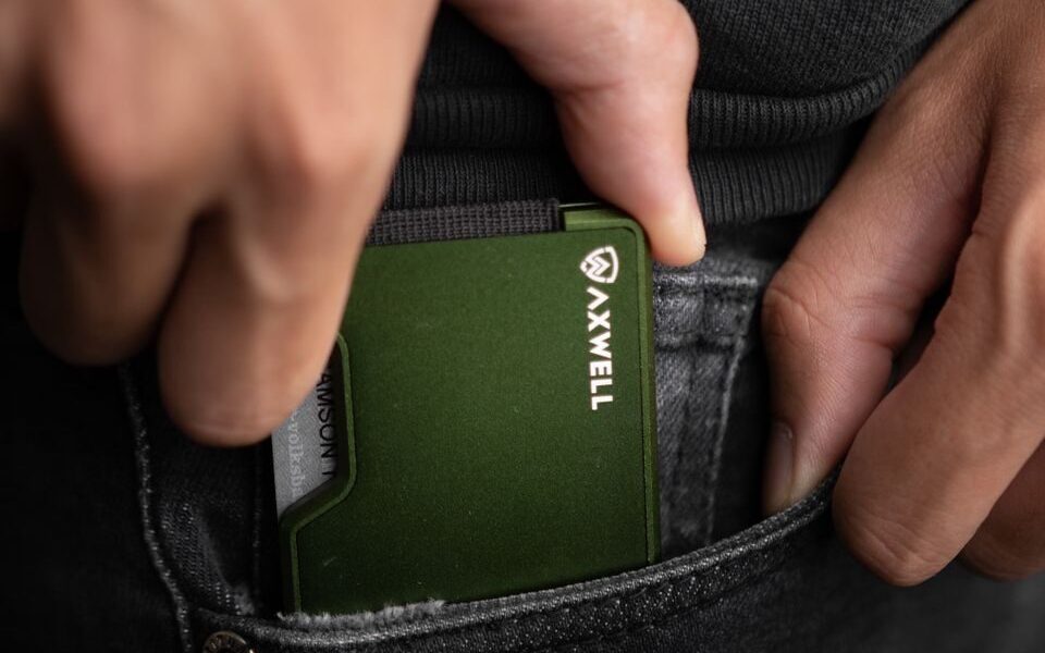 Close-up of a hand holding a minimalist green metal wallet, perfect for everyday carry fashion enthusiasts.