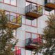 Vertical view of a modern residential block with colorful balconies and trees.