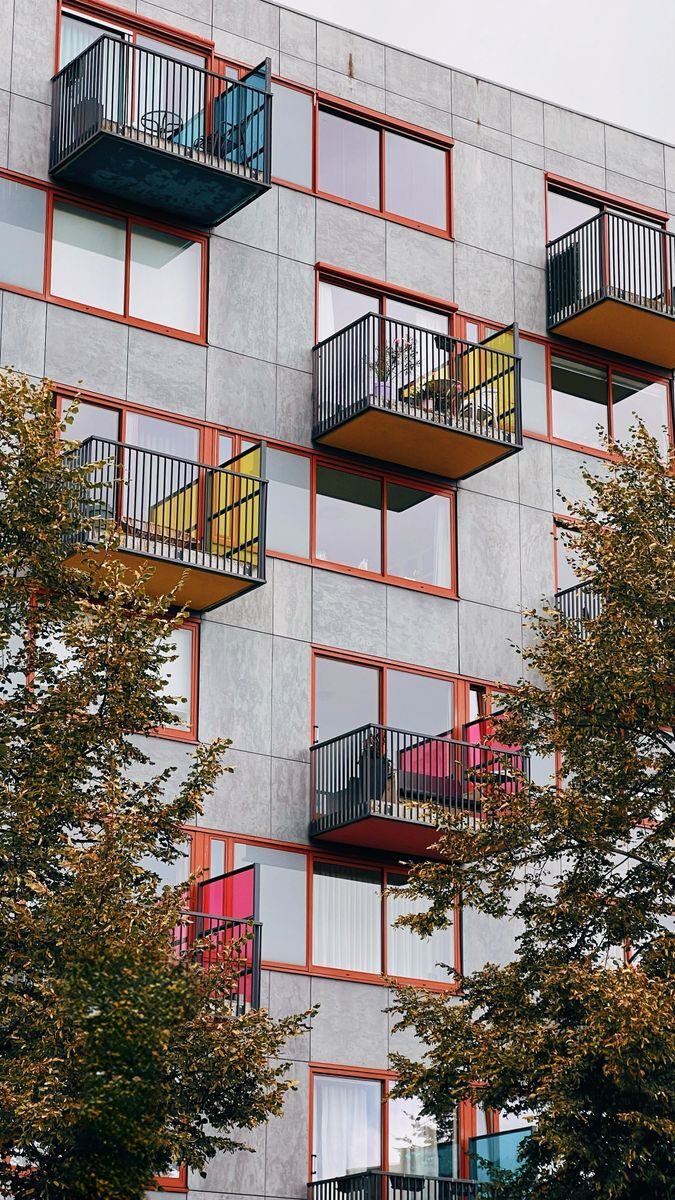Vertical view of a modern residential block with colorful balconies and trees.