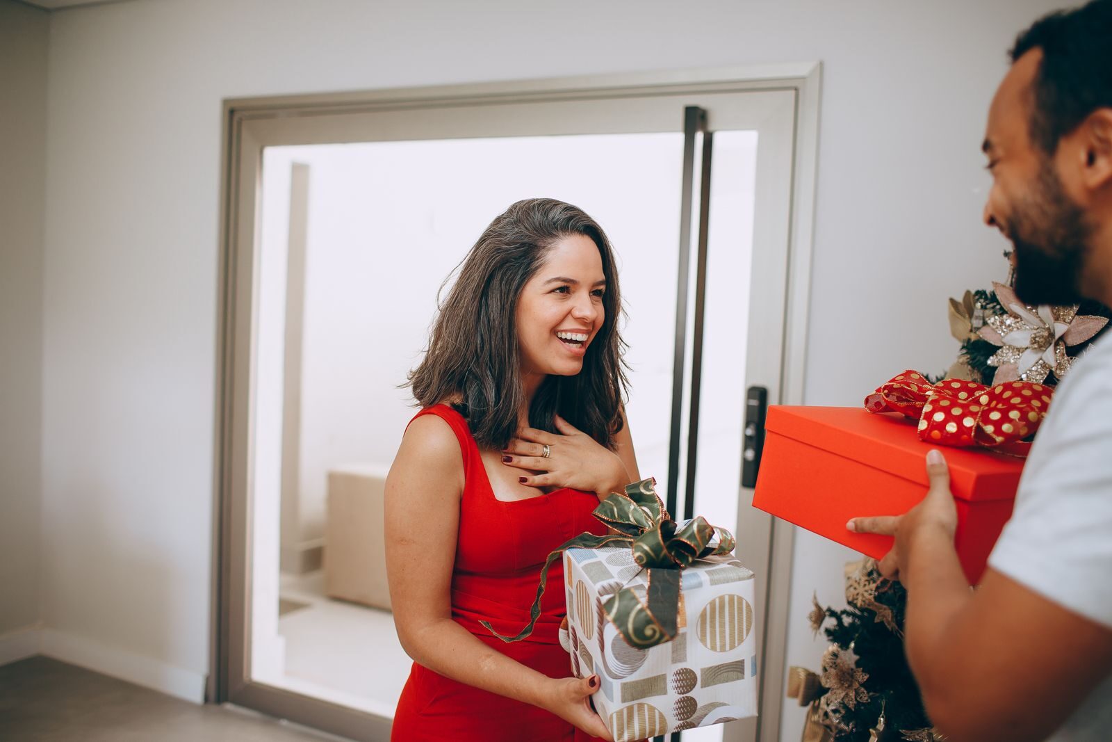 A happy couple exchanging gifts by a Christmas tree in a warm indoor setting.