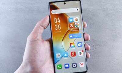 Close-up of a hand holding a smartphone displaying apps on the screen against a textured background.