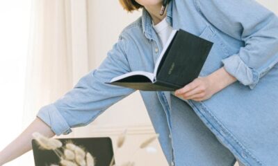 A young woman multitasks with a phone call and notebook in a casual home office setting.