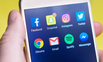 A person's hand holding a smartphone displaying social media and communication apps.