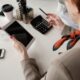 A businesswoman in an office setting holds a tablet while calculating with a pen and calculator on the table.