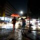 Pedestrians with umbrellas walking in the rain at night on an urban street.