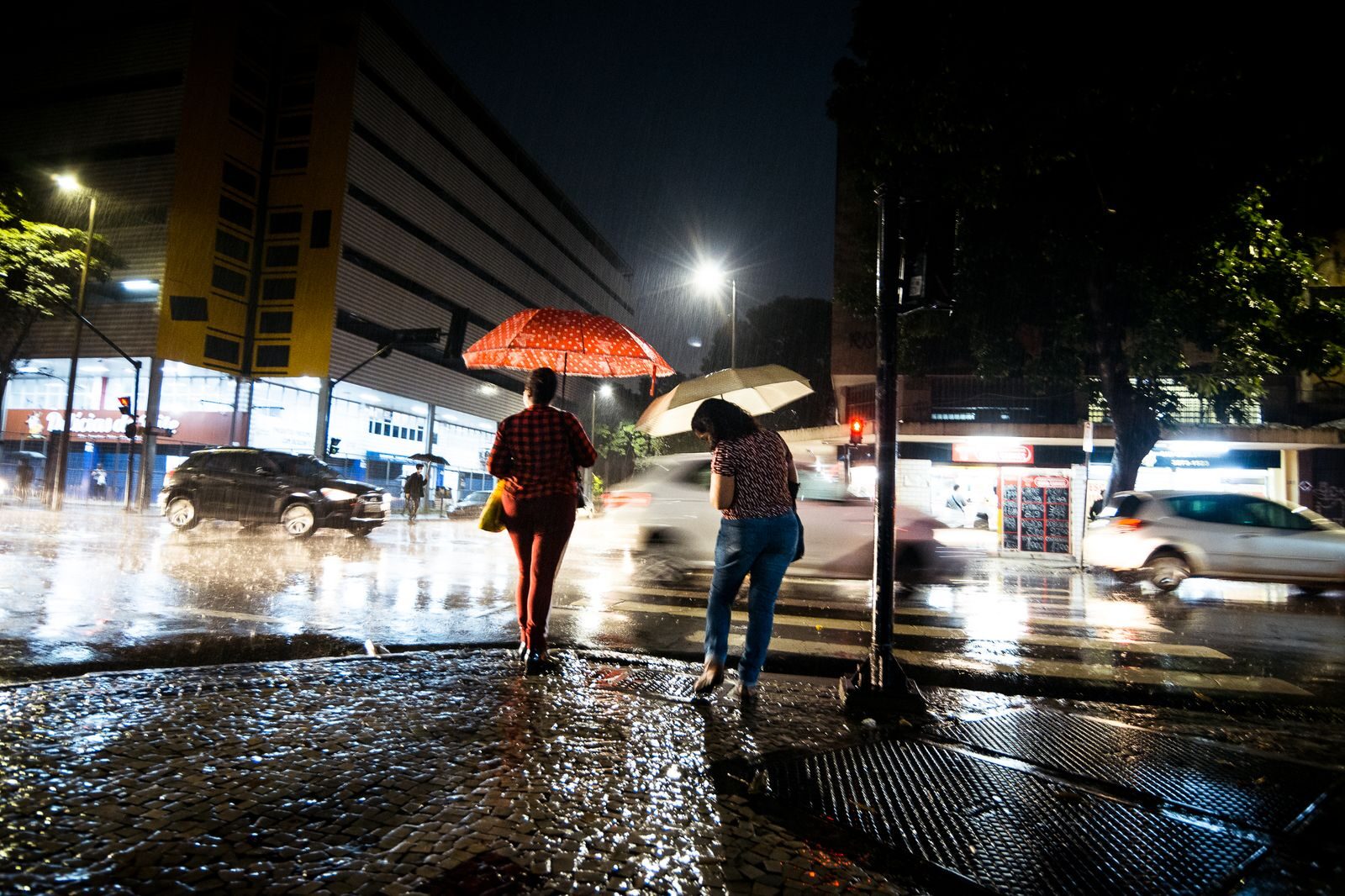 Pedestrians with umbrellas walking in the rain at night on an urban street.