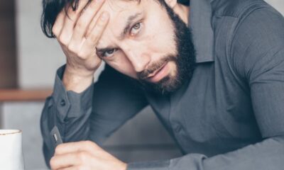 Thoughtful man sitting at a table with glasses and cup, showing frustration.