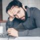 Thoughtful man sitting at a table with glasses and cup, showing frustration.