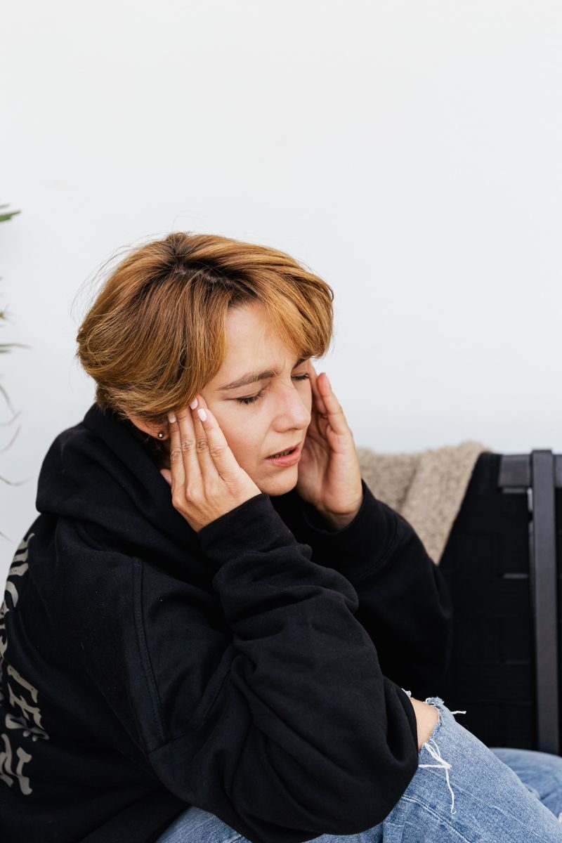 Young woman holding head in discomfort, symbolizing stress or headache.